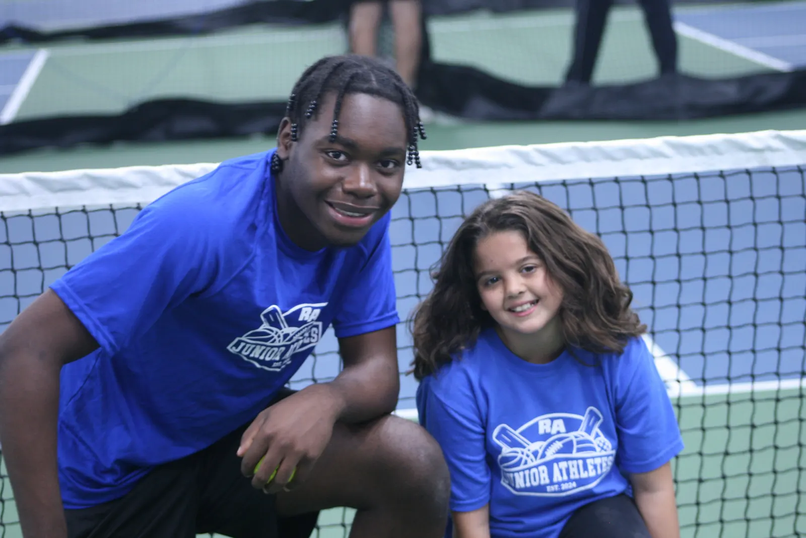 Two Junior Athletes participants smiling on a tennis court